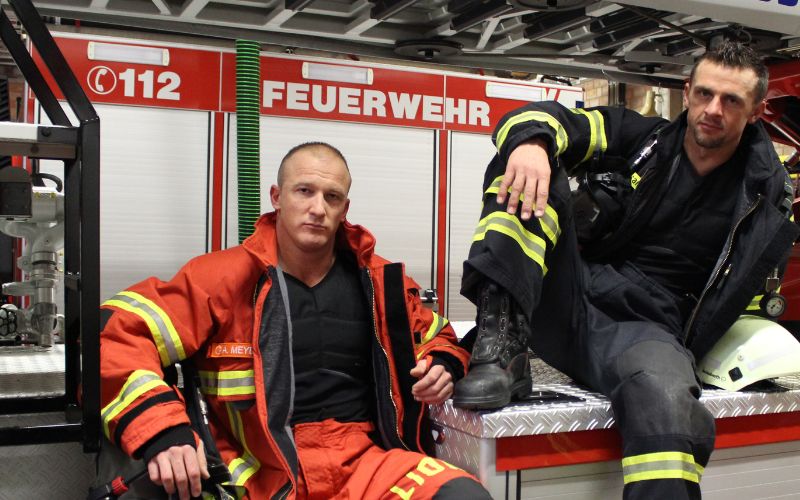 Feuerwehrweltmeister Alexander Mayer und Joachim Posanz mit E.COOLINE Kühlkleidung vor Feuerwehrauto